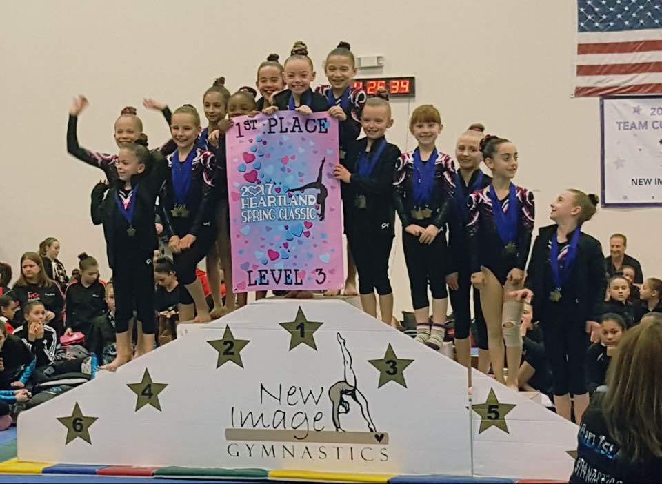 A group of young gymnasts posing with a colorful banner and trophies.