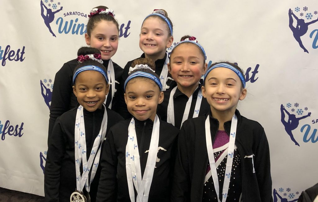 Group of six young gymnasts wearing medals and smiling.