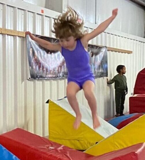 A girl jumping on colorful gym mats inside a gym.
