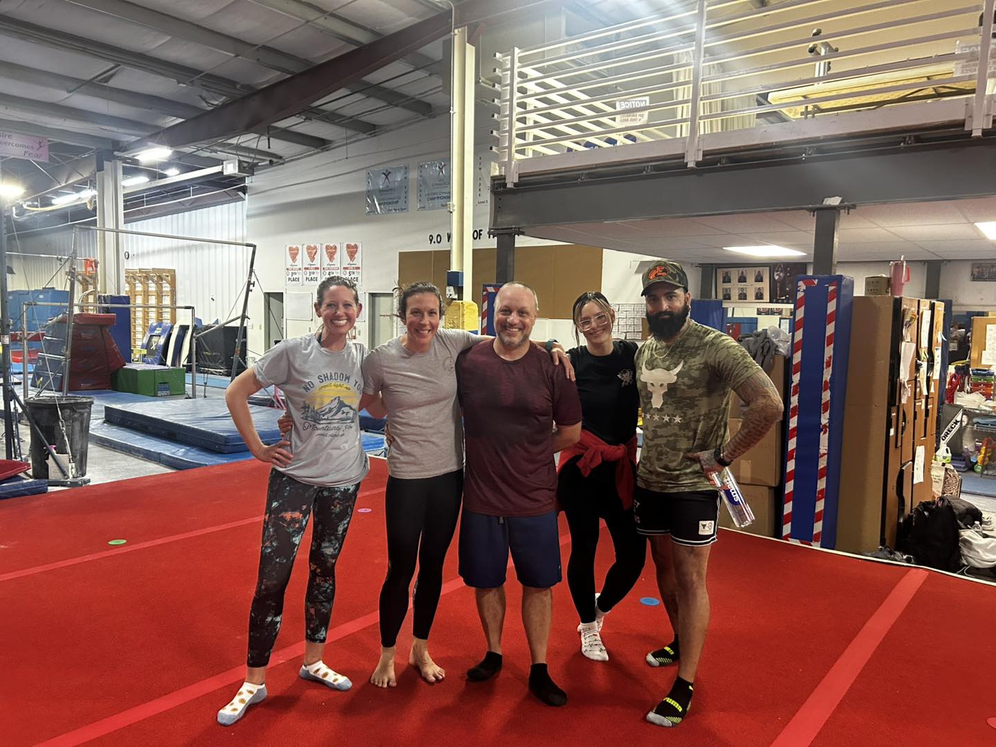 Five men standing together on a red gym floor inside a sports facility.
